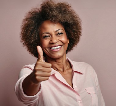 Woman in pink collared shirt giving thumbs up in front of mauve background