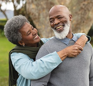 Woman in blue sweater hugging man in gray sweater outside in the grass