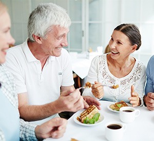 4 people sitting around a white table having pastries and coffee