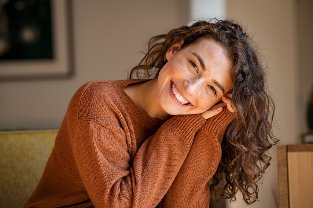 Woman with freckles in brown sweater on the couch smiling